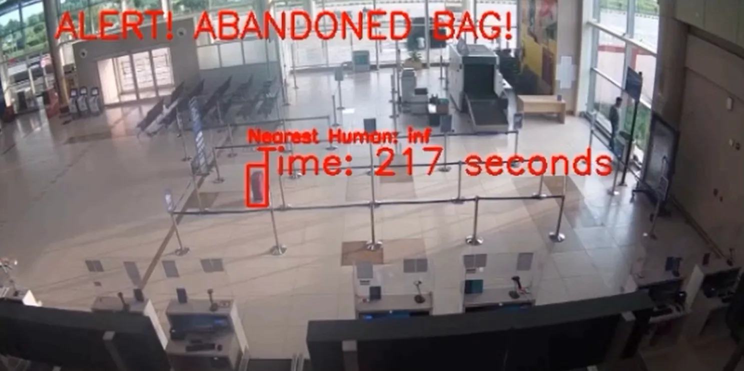Overhead camera view of a terminal hall. A red box marks a suitcase left alone in the queue area.