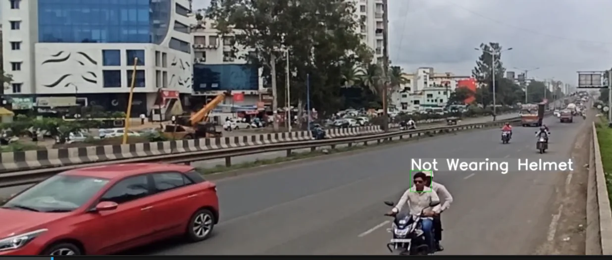 Highway camera view of a motorcycle carrying two people. A green box marks the rider's face under the on-screen label "Not Wearing Helmet".